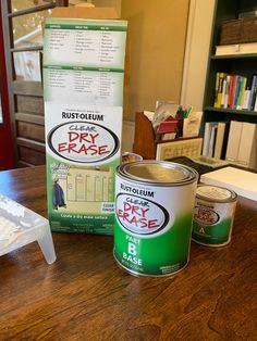 two cans of paint sitting on top of a wooden table next to a package of dry erases