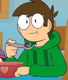 a boy eating cereal from a bowl with a spoon in his hand while wearing a green hoodie