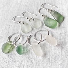 six sea glass dangles in various shapes and sizes on a white surface with silver hooks