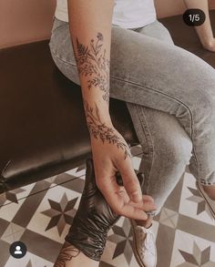 a woman sitting on top of a bench holding her hand up to the side with flowers tattooed on it