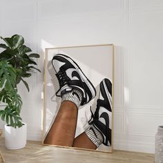 a woman's legs in black and white sneakers on a wooden floor next to a potted plant