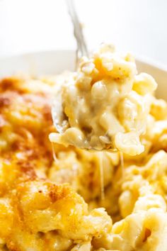 a spoon full of macaroni and cheese being lifted from a white bowl with a fork