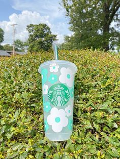 starbucks cup sitting in the middle of a field full of green leaves and bushes, with a straw sticking out of it's top