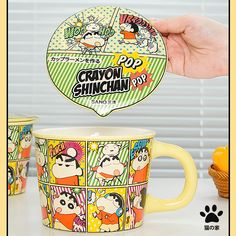 a person holding up a cup with cartoon characters on it and another mug in the background