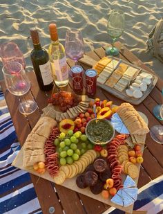 an assortment of food and wine on a picnic table at the beach in front of the ocean