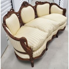 an ornately carved wooden couch sitting in front of a white shuttered wall with shutters