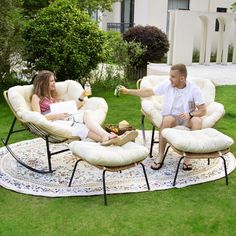 a man and woman sitting on lawn chairs in the grass with drinks, talking to each other