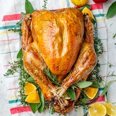 a roasted turkey on a platter with oranges and herbs