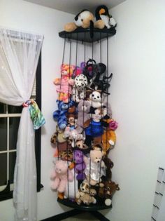 a rack filled with stuffed animals next to a window in a room that has white curtains