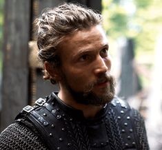 a man with long hair and beard wearing a chain mailed armor looks off into the distance