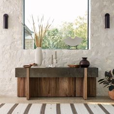 a table with two vases on it in front of a window and a rug