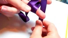 two hands are holding small pieces of purple material on top of a white paper sheet