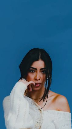 a woman in white sweater posing with her hand on her cheek and looking off to the side