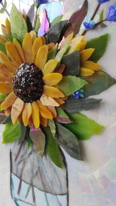 a sunflower is in a glass vase with leaves and flowers on the wall behind it