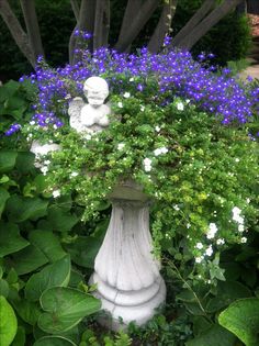 a white statue sitting in the middle of a garden filled with flowers and greenery