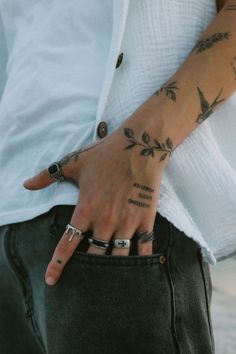 a person with tattoos on their arm and hand holding onto his jeans pocket while wearing a white shirt