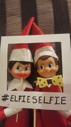 two elfs are holding a sign with the words selfie on it and one is wearing a santa hat