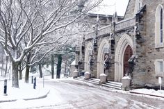 an old church in winter with snow on the ground and trees lining the street near it