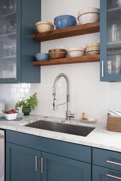 a kitchen with blue cabinets and white counter tops is pictured in this image, there are dishes on the shelves above the sink