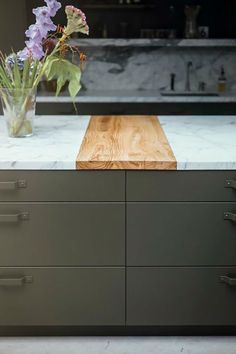 a vase with flowers sitting on top of a kitchen counter next to a wooden cutting board