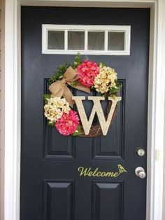 a front door with a welcome sign and flowers on the wreath hanging from it's side