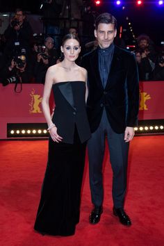 a man and woman standing on top of a red carpet next to each other at an event