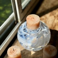 two lit candles sitting on top of a table next to a glass bottle and window