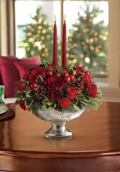 a centerpiece with red flowers and candles on a table in front of a window