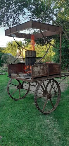 an old wooden cart with a fire in the middle on some green grass and trees