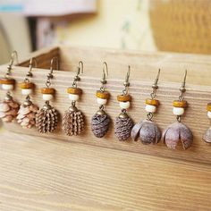 there are many different earrings hanging from the hooks on this wooden board with pine cones and acorns