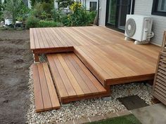 a wooden deck in front of a house with an air conditioner on top of it