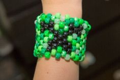 a green and black beaded bracelet on someone's arm with the words beaded minecraft creeper cuff