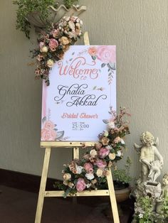 a welcome sign with flowers on it next to a statue and potted planter