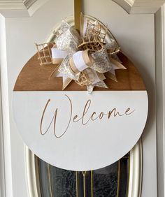 a welcome sign hanging on the front door of a house with gold and white decorations