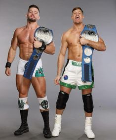 two men standing next to each other holding wrestling belts