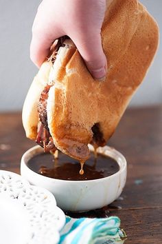 a person dipping sauce into a hot dog in a white cup on a wooden table