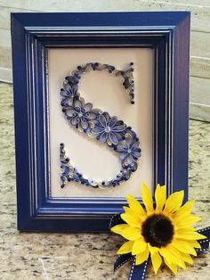 a sunflower is sitting next to a framed letter s with ribbon on the side