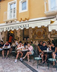 people sitting at tables in front of a building with an artisanal sign on it