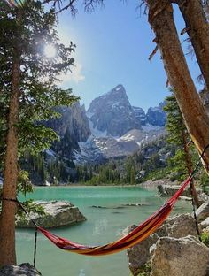 a hammock hanging between two trees in front of a mountain lake with snow capped peaks