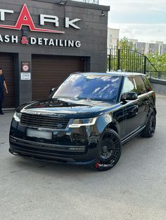 a black range rover is parked in front of a car wash and detailing shop with its door open