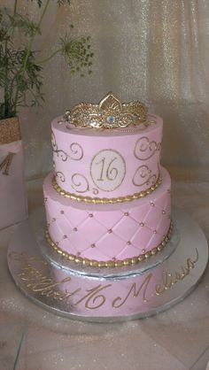 a pink cake with gold decorations and a tiara sits on a silver platter