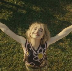 a woman standing on top of a lush green field holding her arms in the air