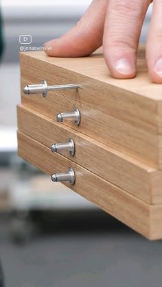 a person's hand is on top of a wooden box with three drawers and four screws