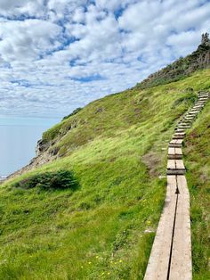 a wooden path going up the side of a grassy hill next to the ocean on a cloudy day