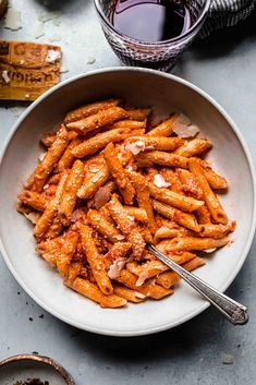 a white bowl filled with pasta and sauce on top of a gray table next to a fork