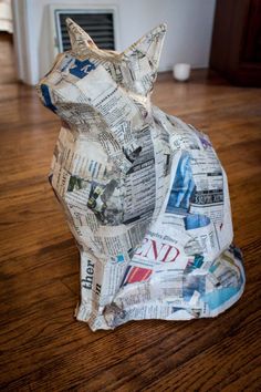 a cat made out of newspaper sitting on top of a wooden floor