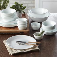 a wooden table topped with white plates and bowls next to a potted green plant