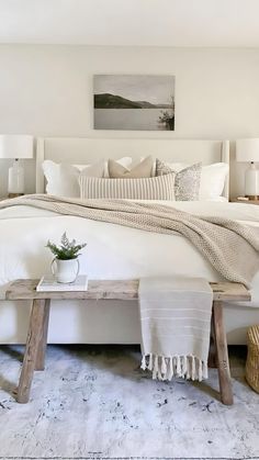 a bed with white linens and pillows in a bedroom next to a painting on the wall