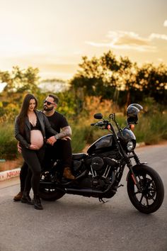 a pregnant woman sitting on the back of a motorcycle with her husband standing next to it