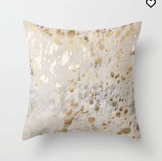 a gold and white pillow on a white wall with some paint splattered on it